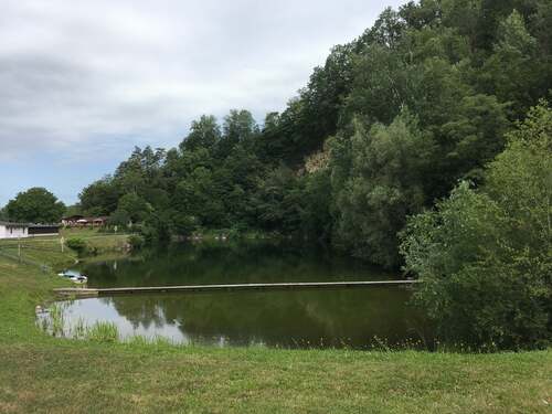 Badeteich im ehemaligen Steinbruch mit bewaldeten Felswänden und einem langen Holzsteg der quer über das Wasser führt