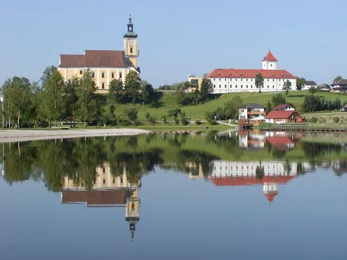 Badesee Waldhausen wo sich auf glatter Oberfläche die Kirche und das Kloster spiegeln