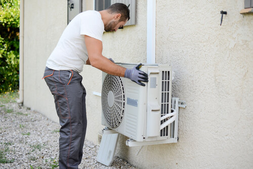 Ein Mann montiert eine Klimaanlage an der Außenseite eines Hauses.