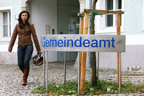 Frau geht an einem Schild mit der Aufschrift 'Gemeindeamt' vorbei