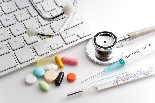 Stethoskop, Einwegspritze, Thermometer und verschiedene Tabletten liegen neben einer Tastatur