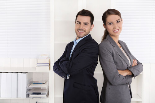 Junge Frau und junger Mann stehen lächelnd in Business-Kleidung Rücken an Rücken aneinander