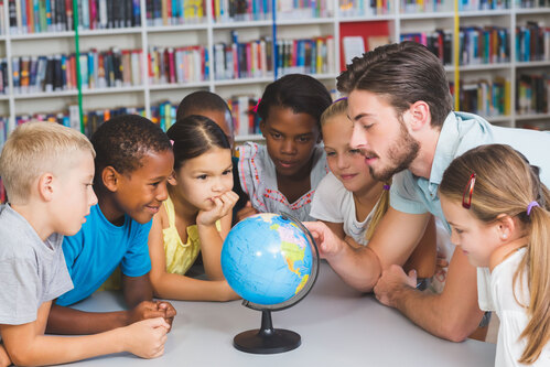 Lehrer zeigt den Schülerinnen und Schüler anhand eines Globus die verschiedenen Länder