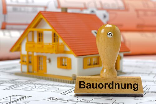 Stempel mit der Aufschrift 'Bauordnung', dahinter steht ein Modellhaus