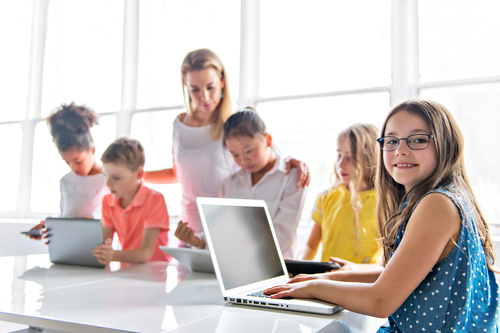 Kinder mit Laptop und Tablet gemeinsam mit Lehrerin im Klassenzimmer