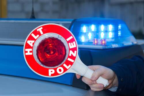 Polizist hält Polizeikelle vor Polizeiauto