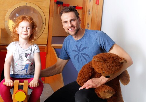 Kindergartenpädagoge mit einem Kind vor einer Rutsche im Kindergarten