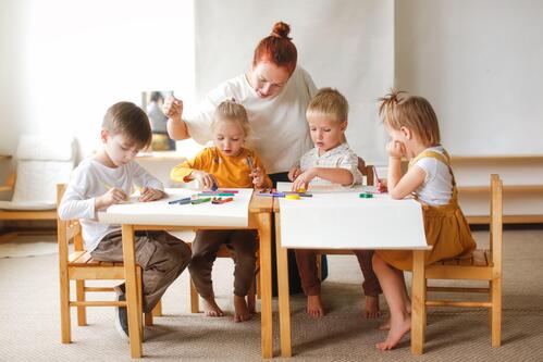 Kindergartenpädagogin mit vier Kindern beim Malen