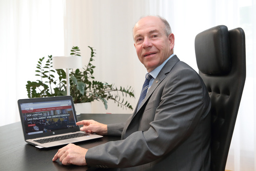 LT-Präsident sitzt einem Schreibtisch, vor ihm ein Notebook, auf dessen Bildschirm die neue Homepage des Oö. Landtags zu sehen ist.
