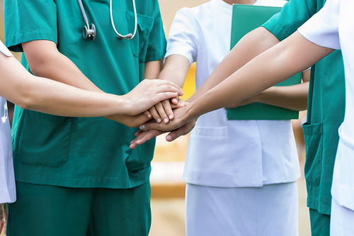 Ärzte und Pflegekräfte legen im Halbkreis stehend als Symbol für ihre Kooperation die Hände aufeinander 