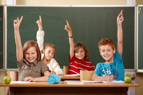 Mehrere Schülerinnen und Schüler sitzen in einem Klassenzimmer und zeigen mit ihren linken oder rechten Armen auf