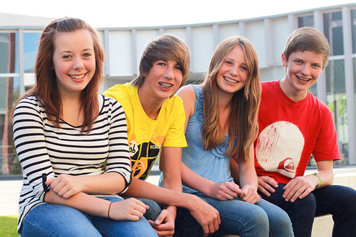 Vier gut gelaunte Jugendliche (zwei Mädchen und zwei Buben) sitzen auf einer Bank