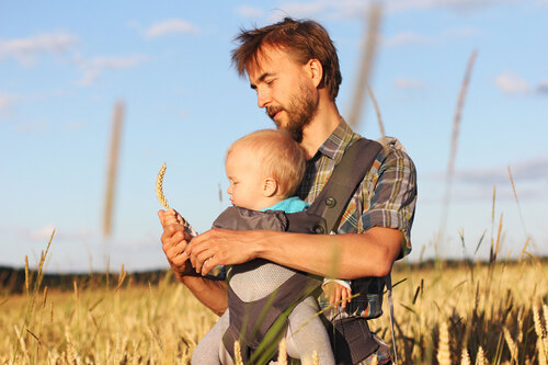 Ein Bauer steht in einem Getreidefeld und zeigt seinem Baby eine Getreideähre.
