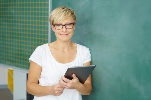 Lächelnde Lehrerin steht mit einem Tablet vor einer Schultafel