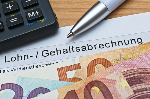Auf einem Lohn- bzw. Gehaltzettel liegen mehrere Euro-Scheine, ein Taschenrechner und ein Kugelschreiber