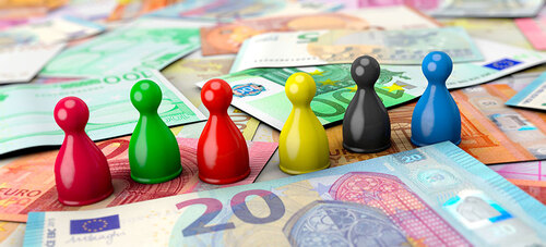 Verschiedenfärbige Kegelfiguren stehen aneinandergereiht auf einem Tisch, auf dem viele Eurobanknoten liegen