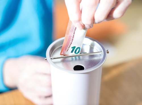 Eine Person steckt einen 10 Euro-Schein in eine Metalldose. 