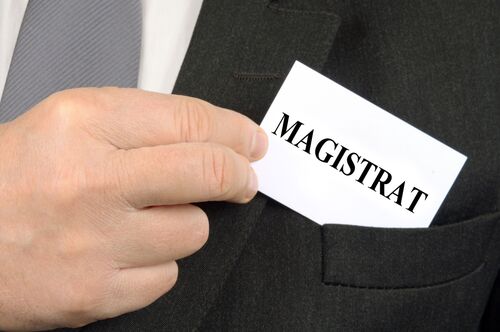 Ein Mann zieht aus der Brusttasche seines Sakkos einen Zettel mit der Aufschrift „Magistrat“.